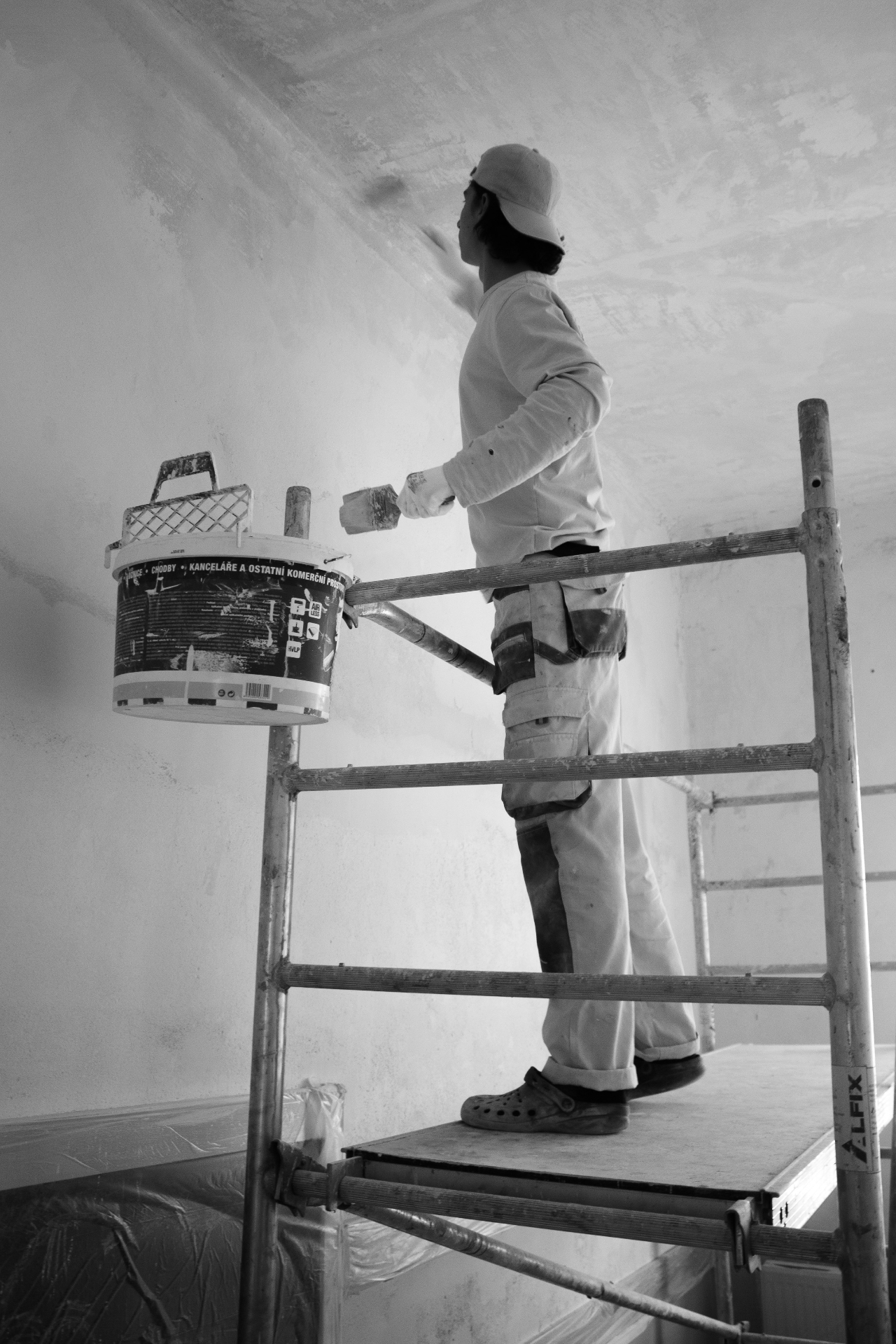 Pintor em andaime a aplicar acabamento numa parede interior