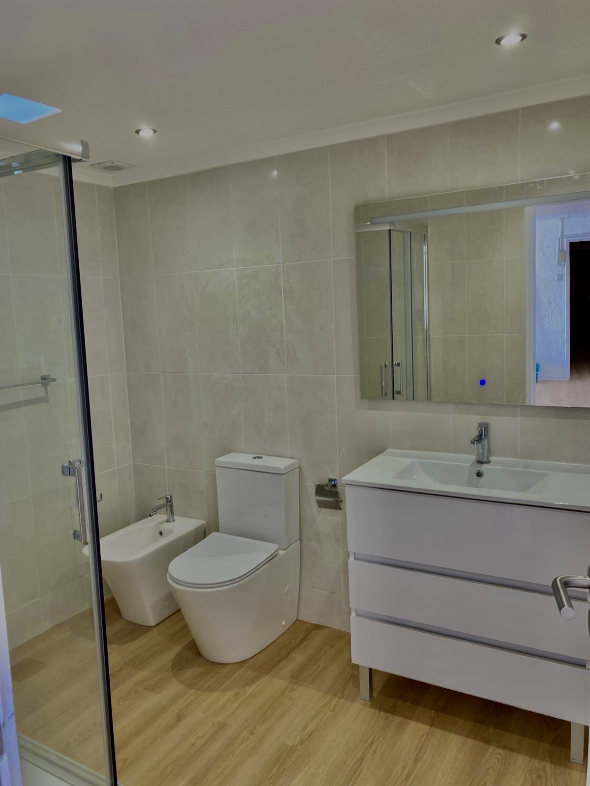 Casa de banho remodelada com móvel branco e pavimento em madeira